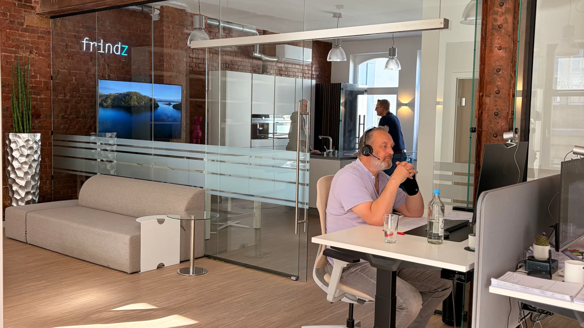 Büro der Frindz GmbH in der Georgstraße in Hannover: Backsteinwand, Glaswand, die Leuchtschrift „frindz“ und ein Mitarbeiter im Innendienst mit Headset.